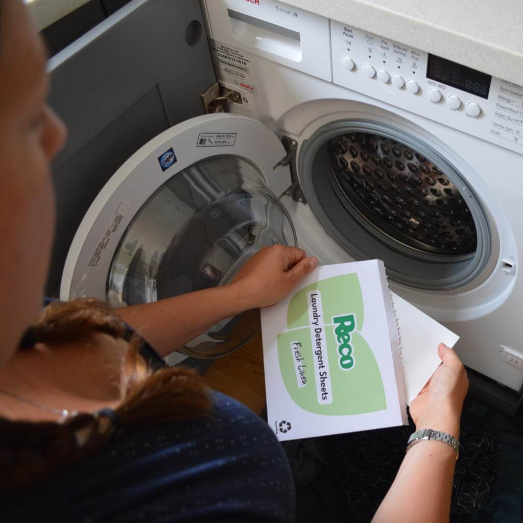 woman holding pack of 10 wash trial pack of Reco Laundry Detergent Sheets in front of washing machine